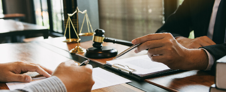 two people in suits looking at papers on a table with the scales of justice and gavel business disputes