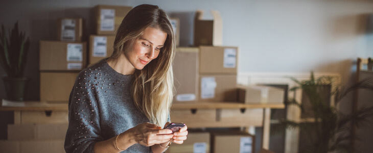 woman looking at her phone, with cardboard package boxes in the background