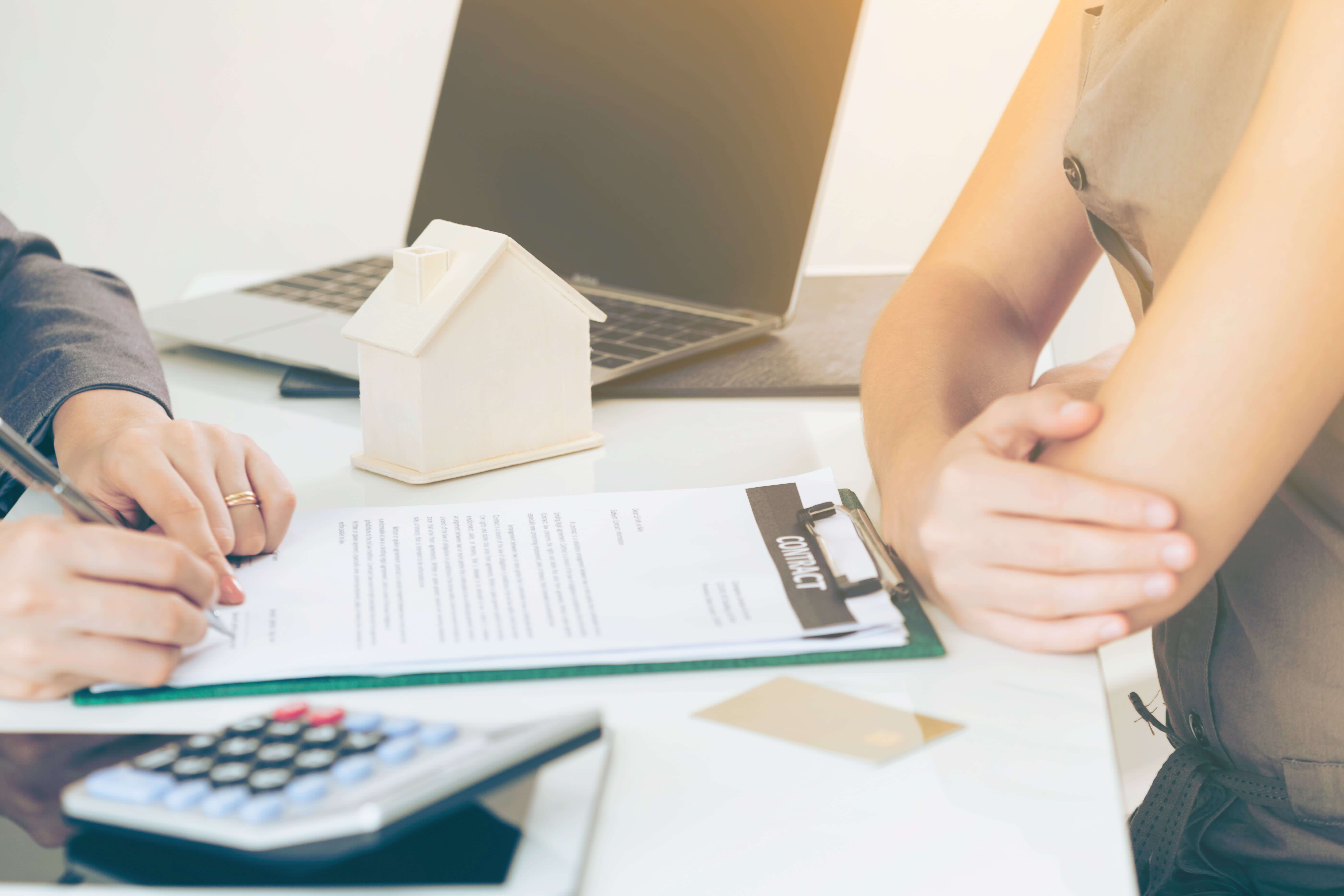 HOA Lawyer Fort Lauderdale, FL-5 two people at a desk preparing to sign a house contract. wooden model of house, laptop, calculator on desk